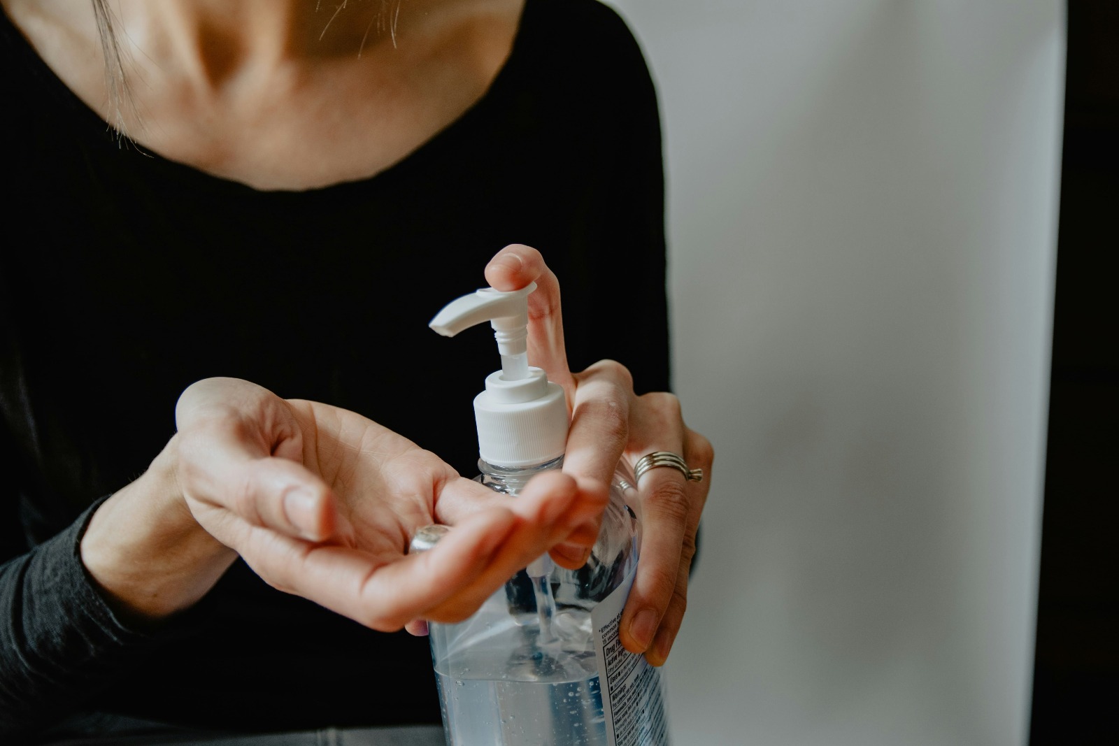 Pessoa aplicando álcool gel nas mãos. O frasco é de apertar e tem rótulo, ele só não está visível. 