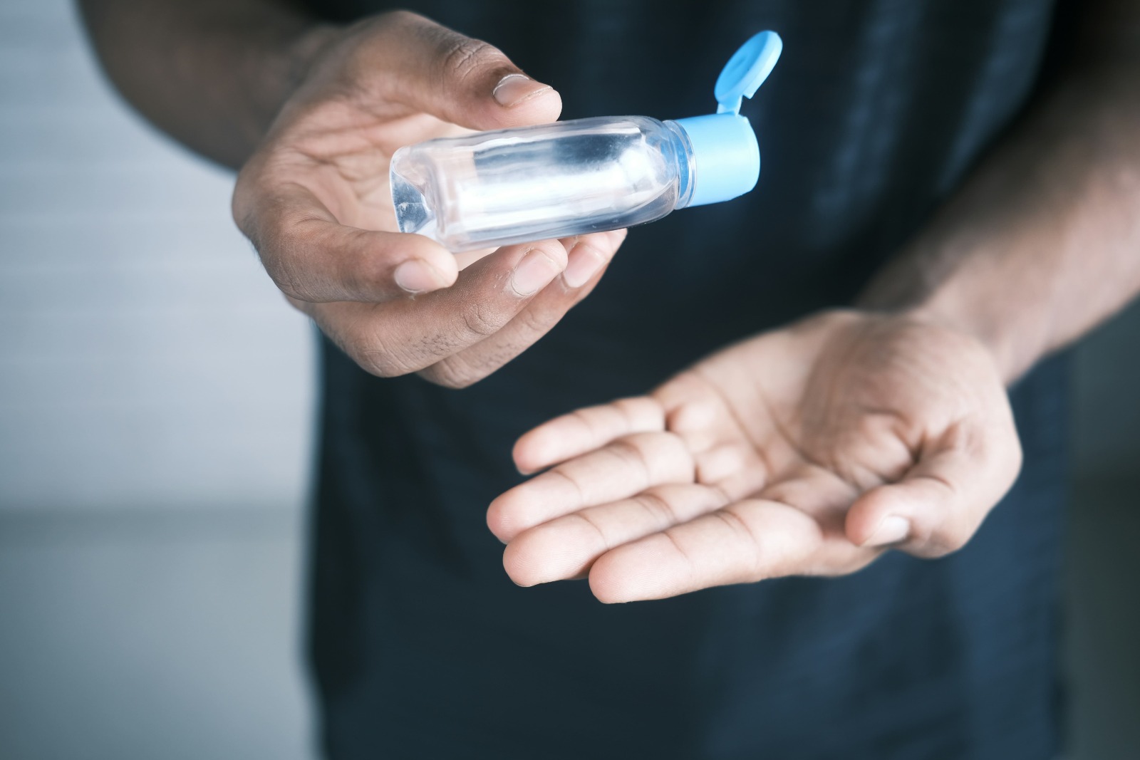 Pessoa aplicando álcool gel nas mãos. O frasco não tem nenhum rótulo. 